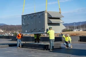 Four men securing a large rectangular unit as it's being lowered onto a roof.