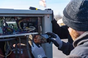Two RBI service technicians viewing real-time visual intelligence reporting on a mobile device while looking inside a rooftop HVAC unit